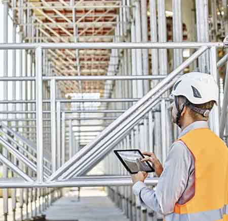Ein Architekt mit Schutzhelm steht mit einem Tablet in der Hand auf einer Baustelle.