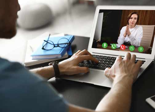Ein Mann sitzt am Schreibtisch mit einem Laptop. Er führt eine Videokonferenz mit einer Frau.