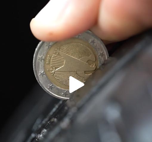 Zwei Finger halten eine Zwei-Euro-Münze ins Reifenprofil.