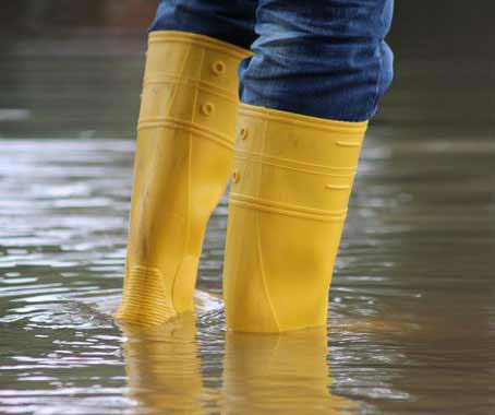 Zwei Beine mit gelben Stiefeln stehen im Hochwasser.