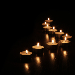 Eine geschwungene Reihe von brennenden Teelichtern steht auf einer dunklen Holzfläche.
