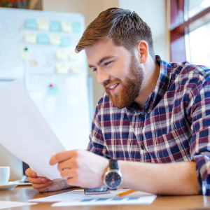 Ein Mann in einem karierten Hemd sitzt im Büro und liest ein Schreiben.