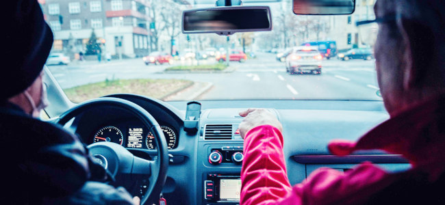 Zwei Personen, Autofahrer und Beifahrer, sitzen in einem Auto und schauen auf den Verkehr.