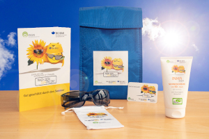 Zusammenstellung des UV-Schutz-Pakets: Sonnencreme, Sonnenbrille mit Beutel, UV-Check-Karte und Informationsmaterial zum UV-Schutz