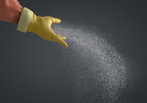 Eine Hand in gelbem Schutzhandschuh  streut staubarme Einstreumittel in Richtung Boden.
