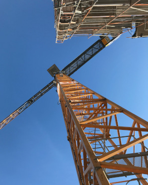 Ein Kran in der Perspektive mit dem Blick hoch zum Kranführer mit blauem Himmel. 