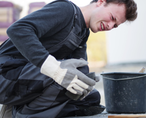 Ein Mann mit Knieschmerzen sitzt am Boden und hält sich sein Knie fest.