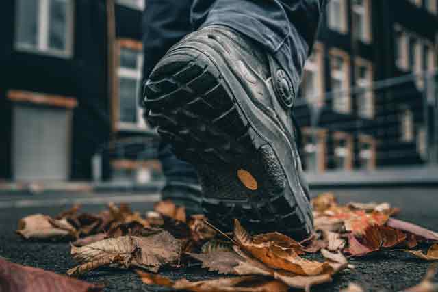 Ein Mensch läuft mit Arbeitsschuhen über Herbstblätter.