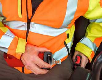 Ein Bauarbeiter ist dabei, sich mit dem Sicherheitsgurt anzuschnallen. Er sitzt in einer Baumaschine.