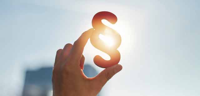 Eine linke Hand hält ein Paragraphen Symbol in die Sonne.