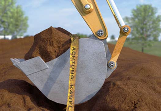 Eine Baggerschaufel hebt Erde aus und reißt dabei ein Kabel beschriftet mit "Achtung Kabel" aus dem Boden. 