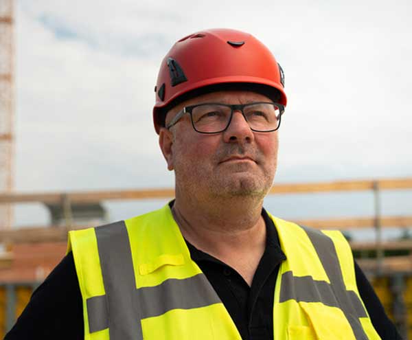 Ein Mann mit Warnweste und Helm schaut in die Ferne.