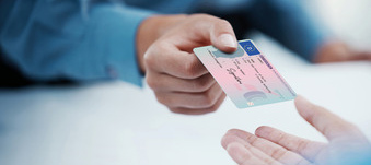 Zwei Hände übergeben einen Führerschein zur Kontrolle.