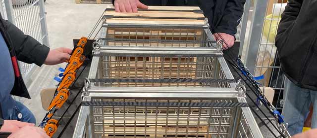 Mehrere Personen sichern Gitterboxen auf einer Ladefläche mit Spanngurten und Ratschen zur fachgerechten Ladungssicherung.
