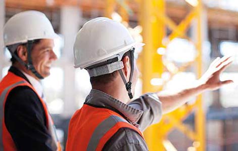 Zwei Bauarbeiter stehen nebeneinander auf einer Baustelle.
