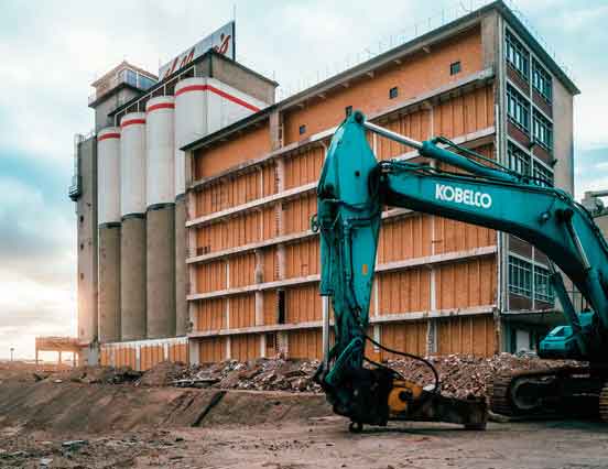 Industriegebäude mit Silos im Rückbau, daneben ein Bagger auf einer Baustelle.