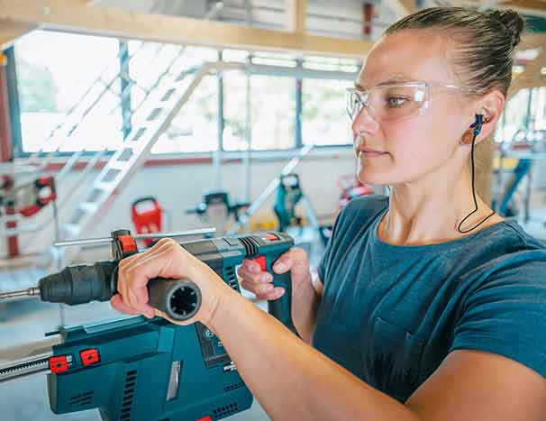 Mann steht auf einer Baustelle und drückt seinen Kapselgehörschutz gegen die Ohren.