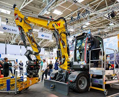 Bagger, der mit einem KI-gestützten Assistenzsystem ausgestattet ist, am bauma-Messestand der BG BAU.