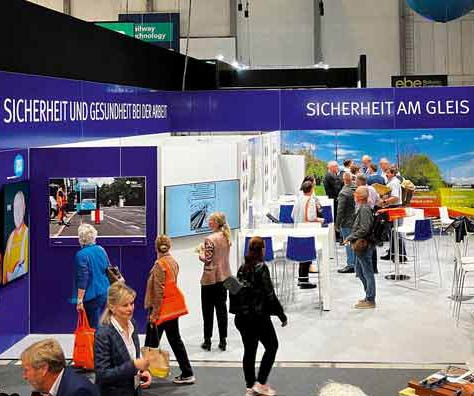 Besucherinnen und Besucher auf einer Fachmesse vor einem Messestand mit der Aufschrift „Sicherheit am Gleis“.