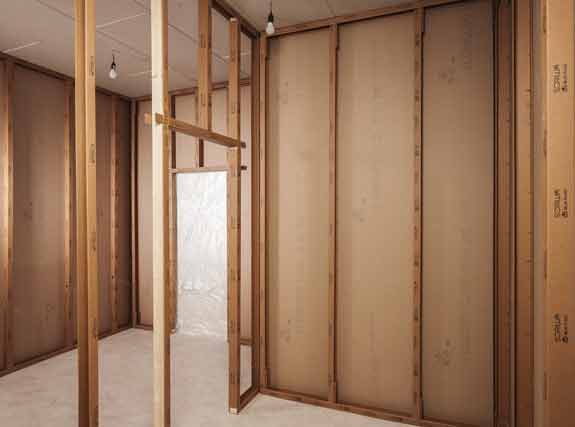 Innenansicht eines Raums im Holzrahmenbau mit freiliegenden Holzständern und Wandplatten im Rohbau.