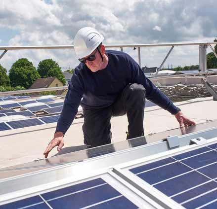 Ein Bauarbeiter mit Schutzhelm arbeitet an einer Photovoltaikanlage auf einem Dach.